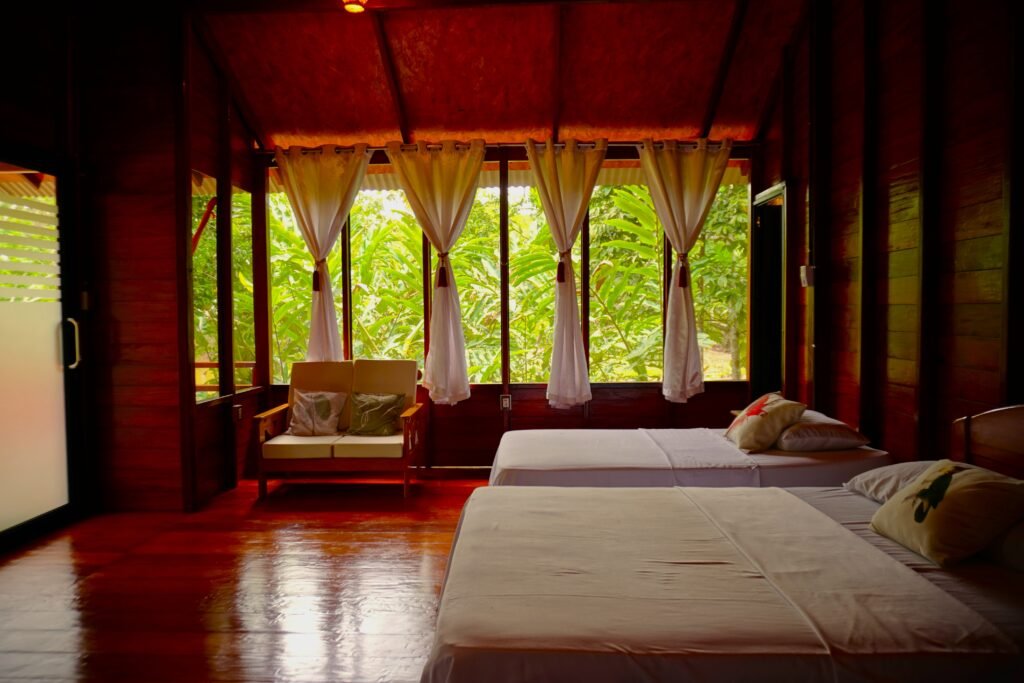 Comfortable wooden cabin interior with twin beds and panoramic windows overlooking the rainforest at a Tambopata jungle lodge